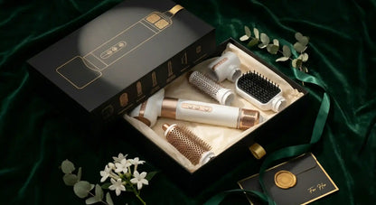 Set of hair care tools including a box, brush, and other accessories on a green fabric background.