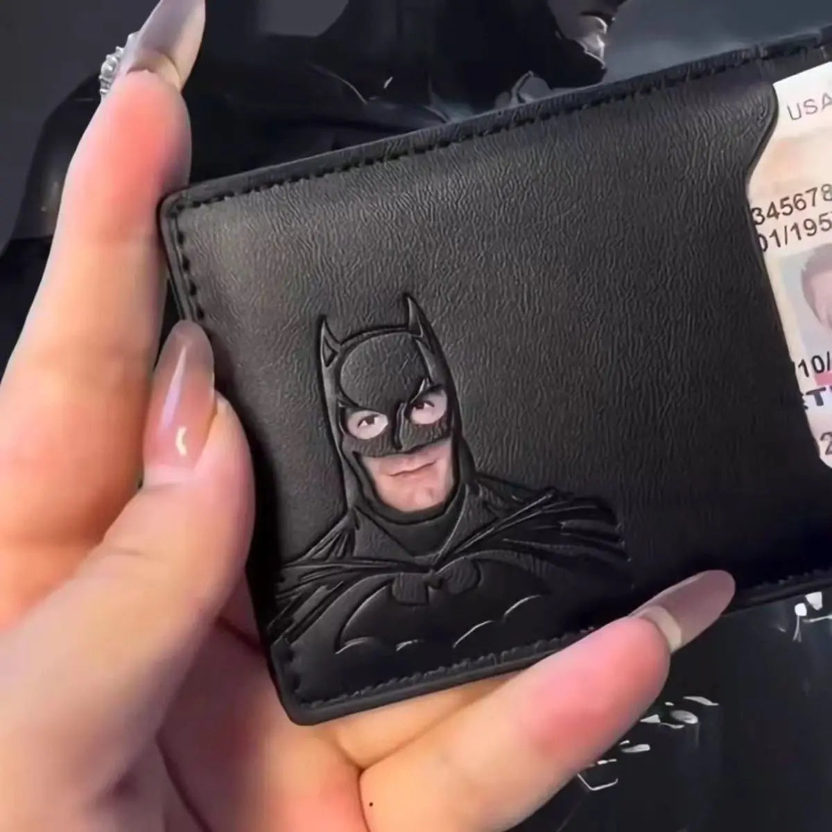 Black leather wallet with a Batman emblem held by a hand.